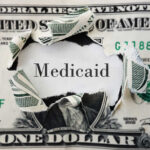 A torn dollar bill revealing the word 'Medicaid'