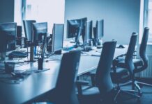 An empty office workspace with multiple computer monitors and chairs