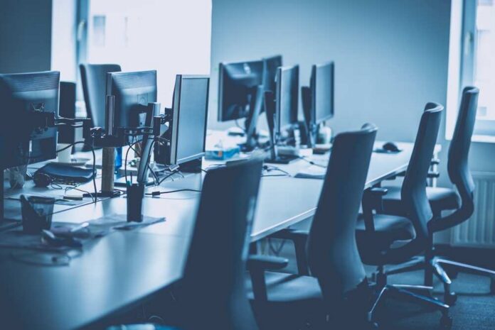 An empty office workspace with multiple computer monitors and chairs