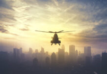 Drug Boat Downed — Where’s The Paper Trail? Silhouette of a helicopter flying over a city skyline at sunset