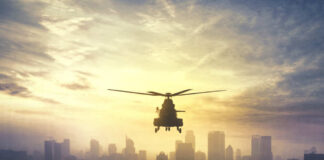 Silhouette of a helicopter flying over a city skyline at sunset
