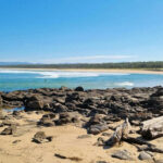Survival Story Raises Questions: Real or Staged? Rocky beach with calm waves and clear blue sky.