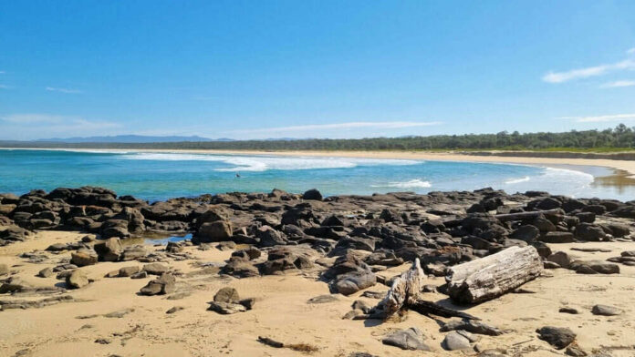 Rocky beach with calm waves and clear blue sky.