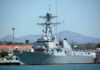 Navy ship docked at harbor with mountains behind