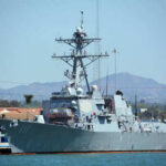 Navy ship docked at harbor with mountains behind