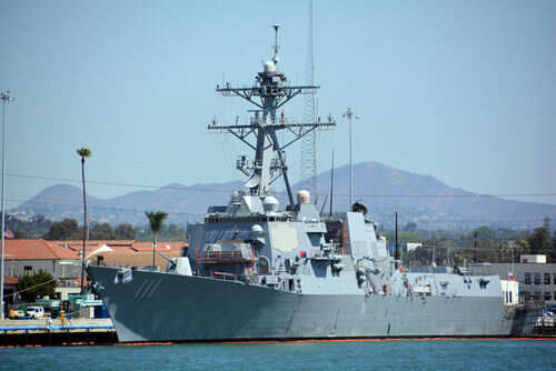Navy ship docked at harbor with mountains behind