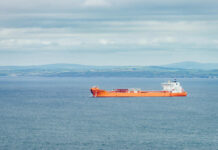 Orange cargo ship sailing on calm sea with distant green hills