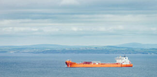 Orange cargo ship sailing on calm sea with distant green hills