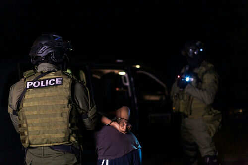 immigration-police-arrest1786607321jpg Two armed officers detaining person at night