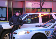 Police officer standing near a crime scene with vehicles and caution tape