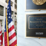 Office plaque beside U.S. and state flags in a government building