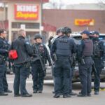 Police officers in tactical gear gather near a patrol SUV