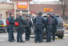 Police officers in tactical gear gather near a patrol SUV