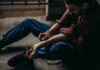 Overdose Survivor Slams America’s Addiction Playbook man sitting on floor injecting his arm with a syringe