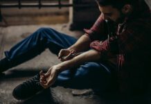 man sitting on floor injecting his arm with a syringe