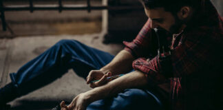 man sitting on floor injecting his arm with a syringe