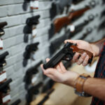 NJ Digs Up Old Therapy To Kill Gun Rights Person holding a handgun in a gun shop with various firearms displayed on the wall