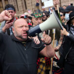 A man shouting into a megaphone during a protest with a crowd in the background