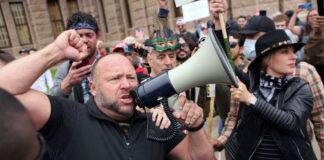A man shouting into a megaphone during a protest with a crowd in the background