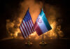 Trump Trades Blocks For Barrels—At What Price? Flags of the United States and Iran displayed on stands with a smoky background