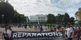 Two individuals holding a banner for reparations in front of the White House