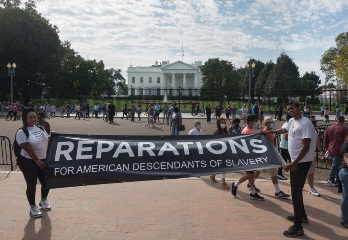 Washington,,Dc,-,Oct.,16,,2021:,White,House,In,Bg, Two individuals holding a banner for reparations in front of the White House