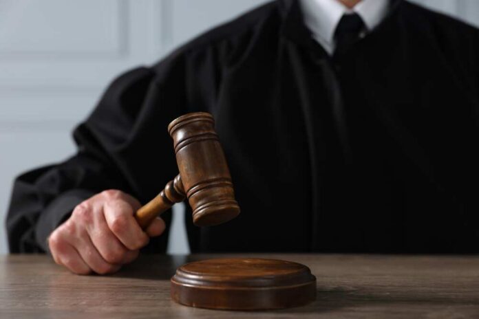 Judge,With,Gavel,Sitting,At,Wooden,Table,,Closeup A judge holding a gavel above a wooden block