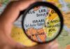 Israel Clash Triggers Tlaib Takedown A hand holding a magnifying glass over a map focusing on Israel