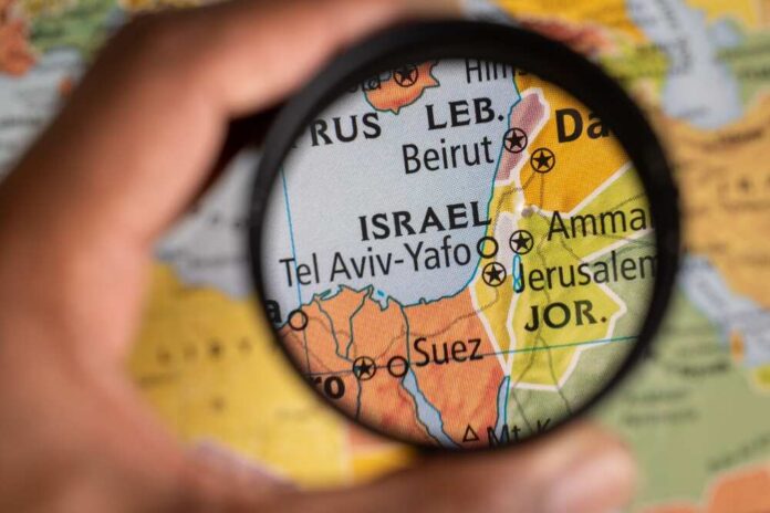Exploring,Israel,Location,On,A,Map,Under,Magnifying,Glass A hand holding a magnifying glass over a map focusing on Israel
