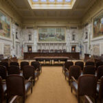 Scotland’s Two-Tier Justice Exposed Interior view of a courtroom with wooden benches and large murals