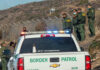 Trump Slams Brakes On ICE Pause Border Patrol officers speaking with individuals near a fence.
