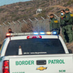 Trump Slams Brakes On ICE Pause Border Patrol officers speaking with individuals near a fence.