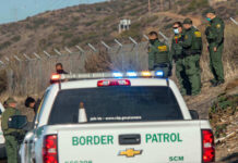 Border Patrol officers speaking with individuals near a fence.