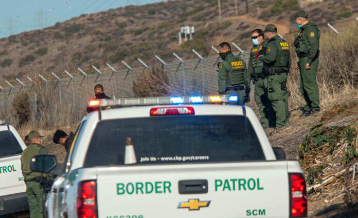 1900868446jpeg Border Patrol officers speaking with individuals near a fence.