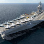 Aircraft carrier sailing at sea with jets lined up on the flight deck