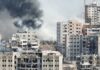 Quake Numbers Explode — What’s Missing? A view of destroyed buildings with smoke rising in the background