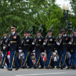 Soldiers in dress uniforms march in formation during a parade