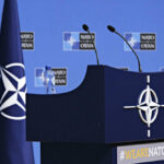 NATO podium with flags and microphones.