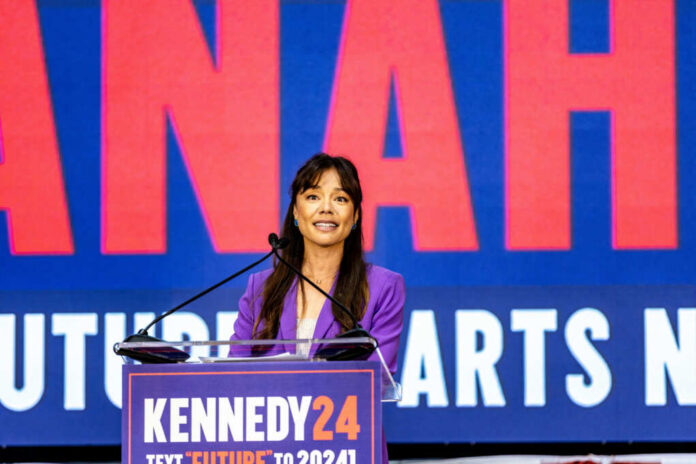 Woman in purple blazer speaking at a podium on stage
