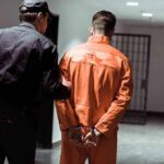 Police officer escorting handcuffed inmate in orange jumpsuit