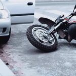 Vigilante Hunt Ends In Murder Motorcycle lying on the street beside a car with an open door