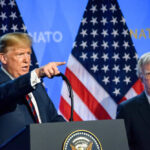 Two men at a press conference with U.S. flags behind them