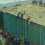 People climbing a tall beachside border fence