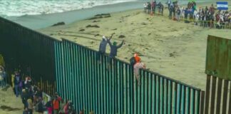 People climbing a tall beachside border fence