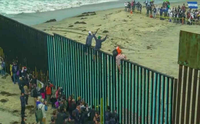 shutterstock_1229072278-1 People climbing a tall beachside border fence