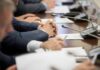 Ghost Budget Exposed: War Bill Ballooning Hands of people in suits at a conference table with microphones