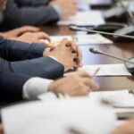 Ghost Budget Exposed: War Bill Ballooning Hands of people in suits at a conference table with microphones