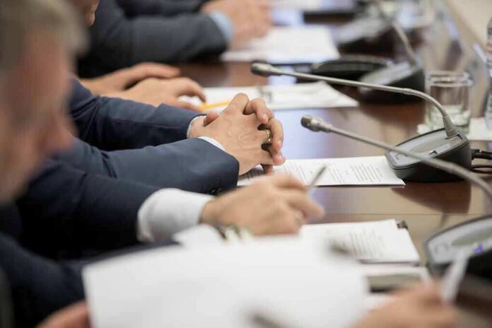 shutterstock_1449056195 Hands of people in suits at a conference table with microphones