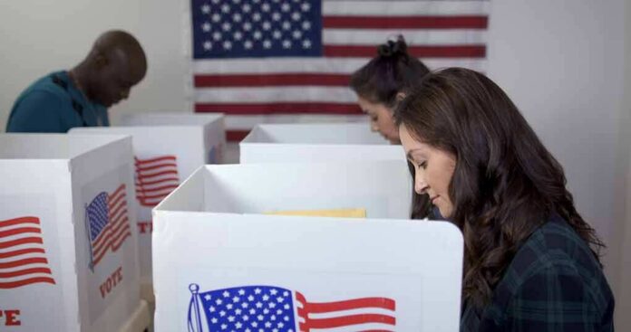 shutterstock_1700215855 Voters at polling booths with American flag in background