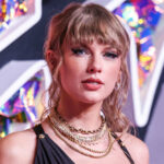 Swift Wedding? Permits Hint, Proof Doesn’t Woman with bangs wearing layered necklaces, colorful background.